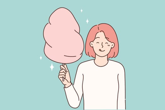 Cheerful girl with cotton candy in hands licks lips in anticipation taste of street dessert