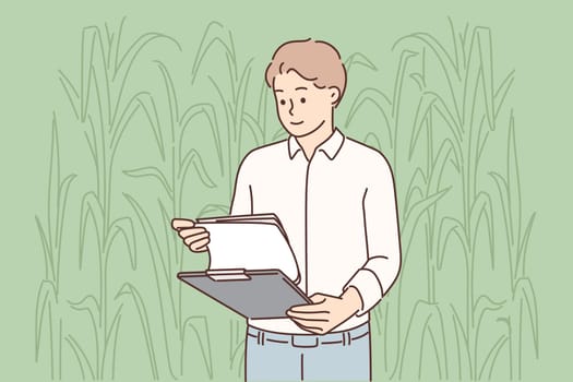 Man farmer inspecting corncobs standing in field with clipboard and working in agribusiness