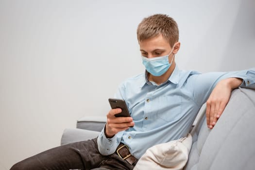 a young man at home on the couch in a mask communicates by video communication on the phone