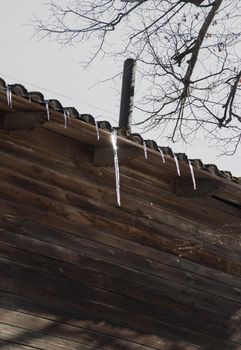 Small icicles hang from the roof of a wooden house and glisten in the sun.
