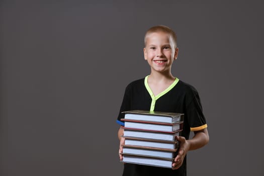 Cheerful boy holding a stack of books on a gray background