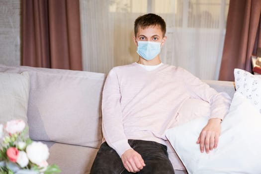 a young guy in a shirt and a protective mask sits on the couch