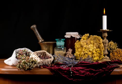 Close up of healing herbs alchemist stuff. Old pharmacy, alternative medicine concept. Dried healing herbs, flowers and candles, ritual purification , copyspace mortar and pestle. on a black background. wooden table.