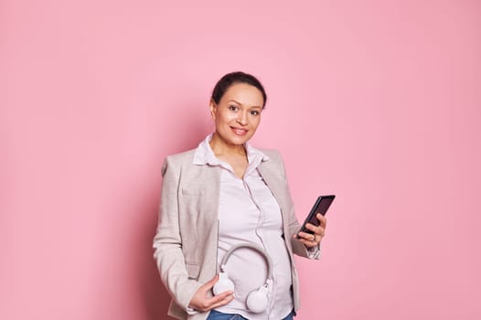 Pregnant woman with headphones on her belly, puts some classical music on playlist in mobile application on a smartphone