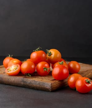 Bunch of ripe red cherry tomatoes on a wooden board, black background