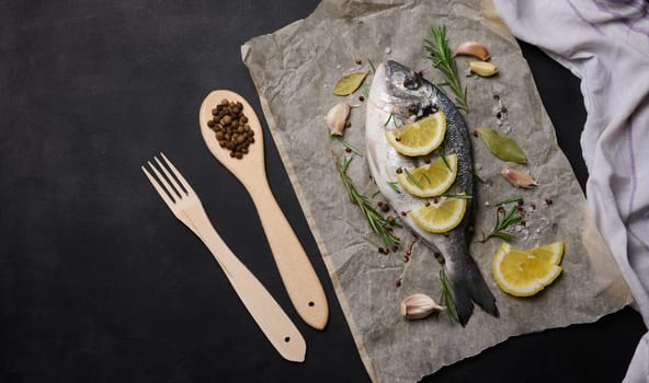 Raw whole dorado fish on brown parchment paper and spices for cooking, top view on black table