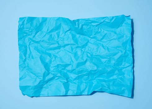 Crumpled rectangular sheet of blue paper on a blue background, top view. Place for inscription
