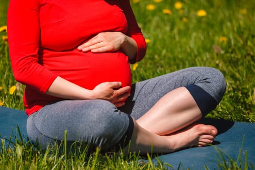 Pregnant woman doing asana Sukhasana outdoors on grass