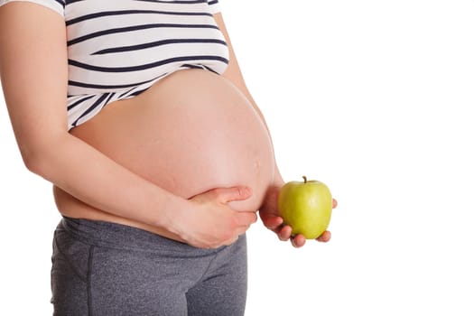 Pregnant woman standing and holding apple near her stomach