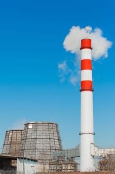 Pollution of the environment, ecology and air. Withdrawal of combustion products of soot, smoke and gases from the pipe and cooling tower of an industrial plant into the atmosphere against the background of a blue sky