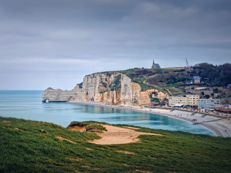 Sightseeing view to Etretat coastline with the famous Notre-Dame de la Garde chapel on the Amont cliff. Seashore washed by Atlantic ocean waters, Normandy, France