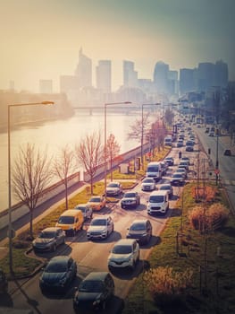 Busy traffic on highway and city streets creating high pollution and smog. Urban sunset view across Seine river to La Defense metropolitan district, Paris, France