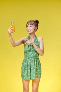 Excited asian woman drinking beverage freshness orange juice glass standing on yellow background