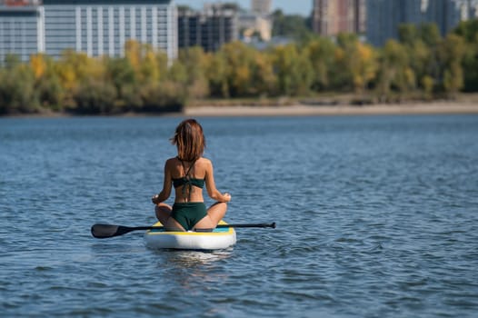 Caucasian woman is riding a SUP board on the river in the city. Summer sport.