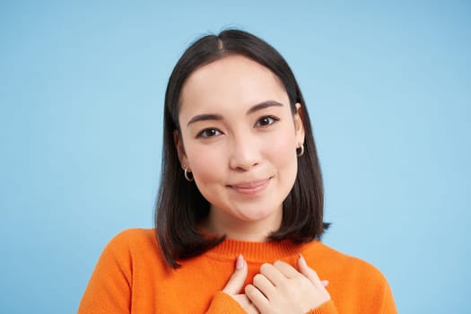 Close up portrait of beautiful korean woman with healthy smile, natural clear facial skin, stands over blue background