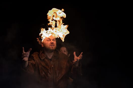 Bald man in a leather jacket with a burning head on a dark background.