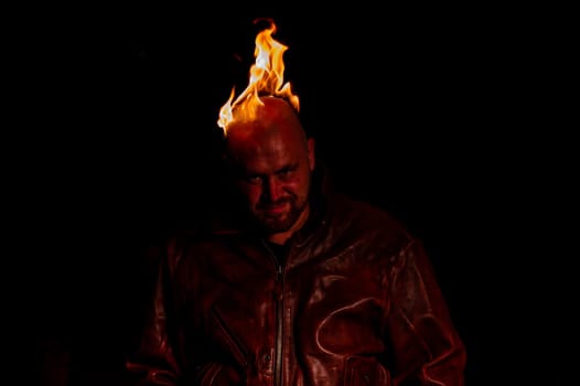 A bald man in a leather jacket with a burning head grins.
