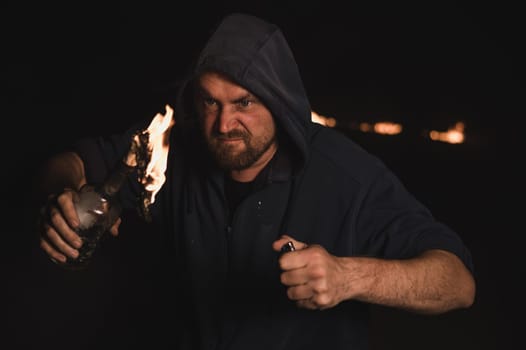 The man in the hood is holding a burning bottle. Molotov cocktail.
