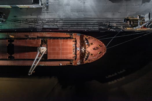 A transport ship docked at night in a harbour ready to load goods for shipping
