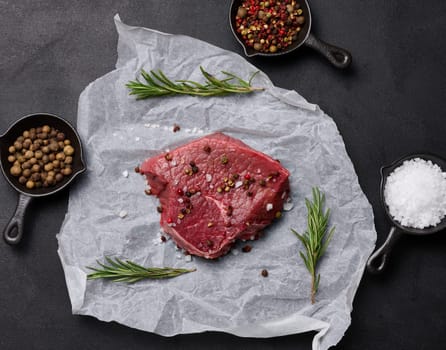 Raw piece of beef with spices lies on a white piece of parchment paper, top view