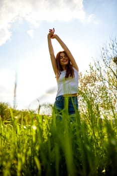 joyful slender woman posing in a field with her arms raised high