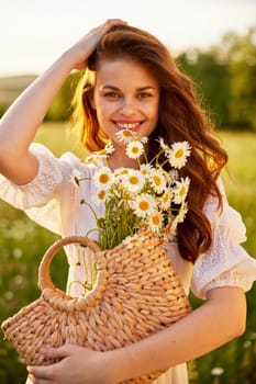 beautiful red-haired woman in a light dress with a basket of daisies in nature in the rays of the setting sun