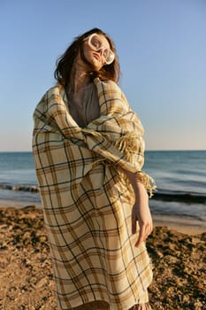 cute woman stands with a plaid during sunset on the beach. Rest, enjoyment