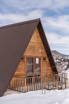 A vertical shot of a wooden cottage surrounded by snow. A recreation area in the mountains