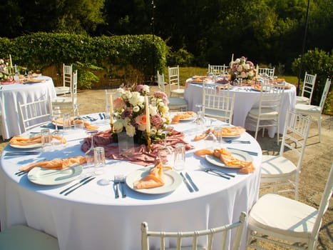 Wedding banquet concept. Chairs and round table for guests, served with cutler and, flowers and crockery and covered with a tablecloth