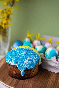 Easter composition with yellow-blue Easter cakes, sprinkles, Easter multi-colored eggs. wooden stand and spring flowers on a yellow background. copy space
