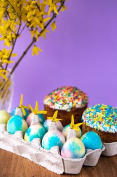 Easter cake on a purple background with yellow spring flowers. easter colored eggs. Easter food. minimal concept.