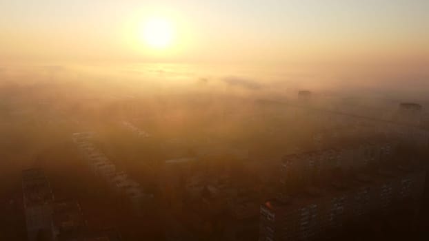 Bright shining sun at dawn, fog over rooftops of multi-storey buildings.