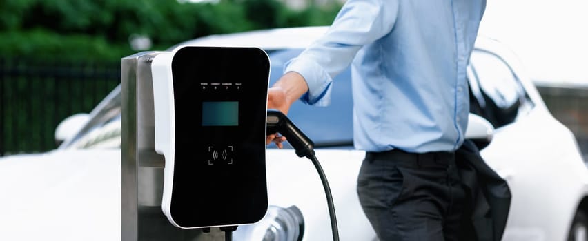 Closeup progressive businessman with electric vehicle at charging station.