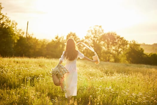 a woman in a light dress stands in a field in the warm rays of the setting sun holding a hat over her head