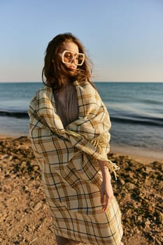 cute woman stands with a plaid during sunset on the beach. Rest, enjoyment
