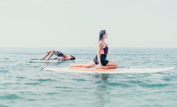 Woman sup yoga. Happy young sporty woman practising yoga pilates on paddle sup surfboard. Female stretching doing workout on sea water. Modern individual female outdoor summer sport activity.