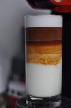 Vertical closeup of three-layer latte macchiato in a tall glass