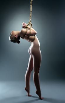 Studio shot of flexible nude girl hanging on rope