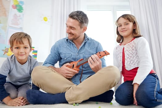 Dad always makes time to play. a happy father playing the guitar for his son and daughter at home.