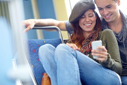 Technology bringing people closer together. a happy couple on the train looking at something on a cellphone