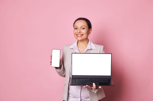 Pleasant pregnant businesswoman shows smartphone and laptop with white digital screen with mockup for ads or mobile apps