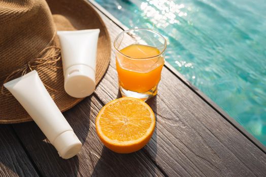 Orange juice, straw hat, sunblock and sunglasses by poolside