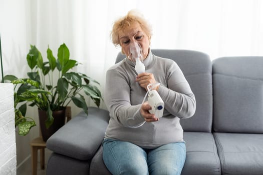 Senior woman using a nebulizer makes inhalation at home and looks at the camera