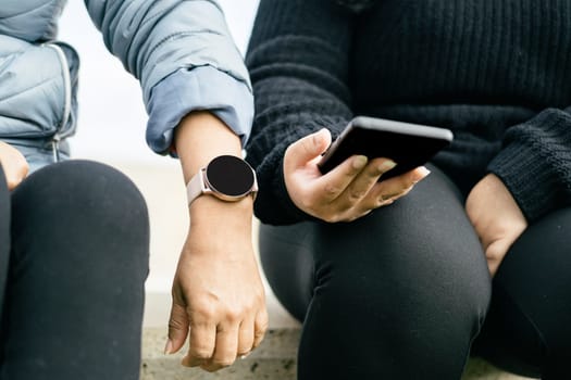 two beautiful Latina women are proudly displaying their new smartwatch and smartphone. Hispanic ladies are keeping up with the latest technology trends