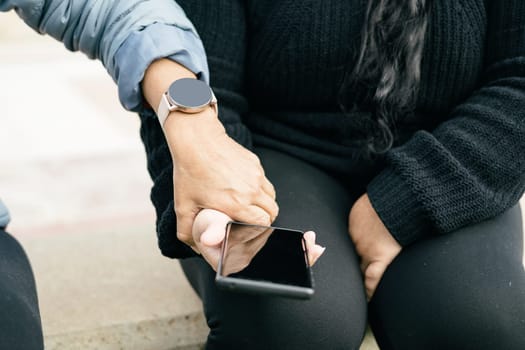 Two Spanish-Latin women with smartphones and smartwatches, selective focus on the clipped hands.