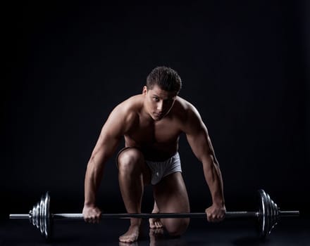 Sexual muscular guy posing with barbell in studio