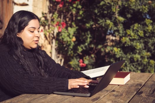 latin woman with long dark hair, working outdoors with laptop