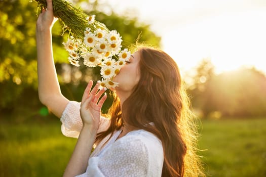 close portrait of a red-haired woman in a light dress sniffing a bouquet of daisies. nature, sunny weather. High quality photo