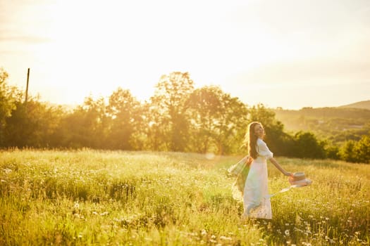 a woman in a light dress with a hat in her hands is spinning in nature in the rays of the setting sun