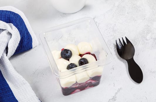 Dessert of cream, jam and blueberries in a plastic glass on a concrete background.